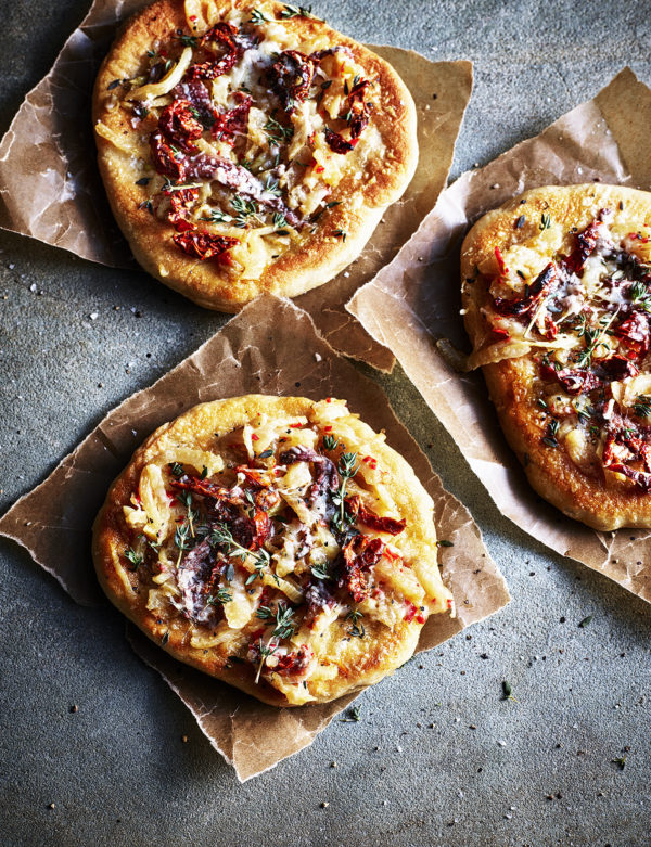 Food photography showing flat breads, topped with red onion and sun dried tomatoes