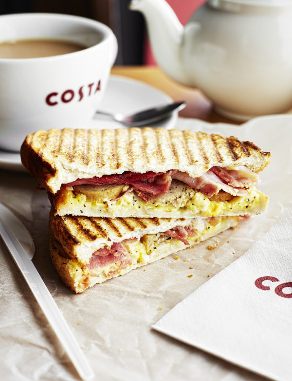 Food photography showing a classic breakfast toastie containing bacon, egg and sausage, with a Costa cup with a hot drink on the side