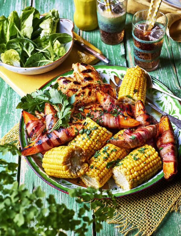 Food product photography showing a plate of BBQ chicken with corn on the cob, along with a side salad and two classes of coke.